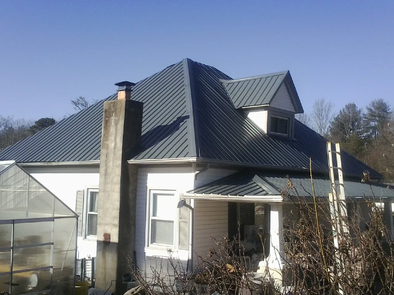 Dark blue standing seam metal roof on a white farmhouse with dormer — Slate & Tile Roof Repair by Roofing Brothers in East Greenwich