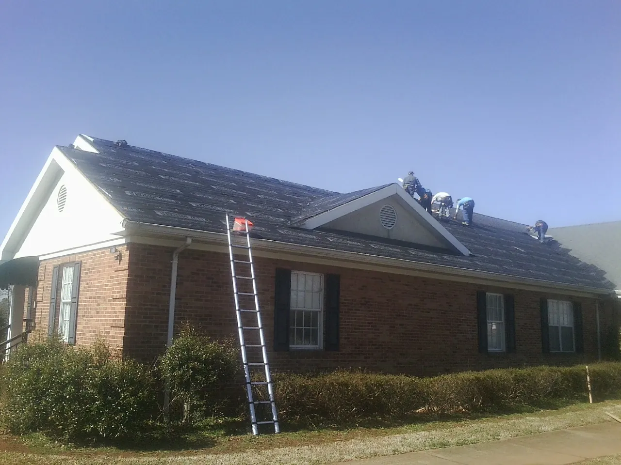 Crew tearing shingles off a brick ranch roof with a ladder set — Metal Roof Repair work by our crew in East Greenwich