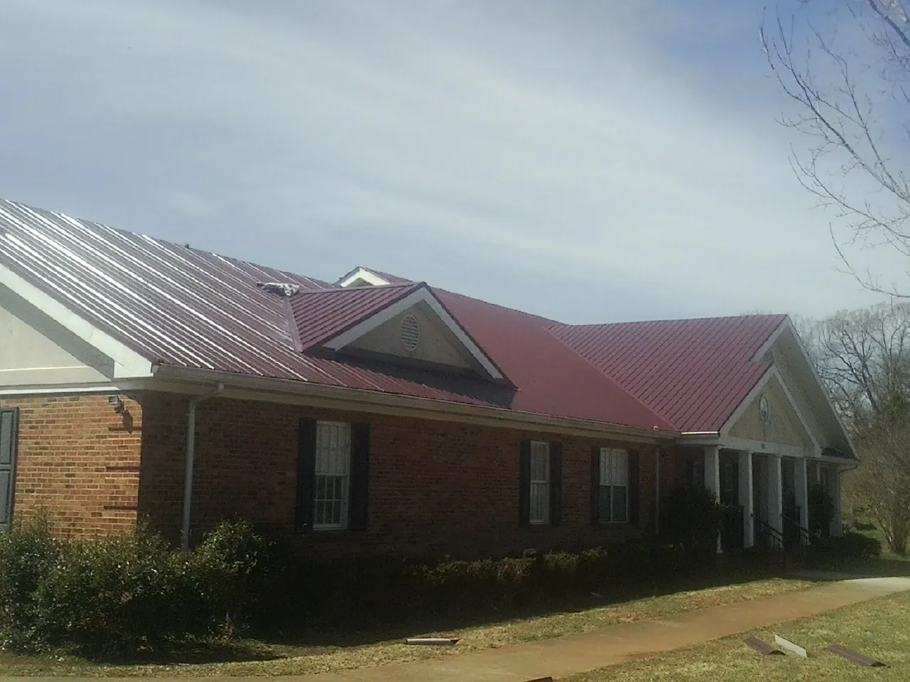 Red metal roof with gabled entries on a long brick building, from a Hail Damage Roof Repair job in East Greenwich