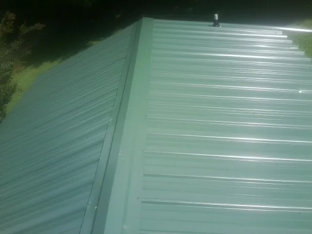 New green metal panels meeting at the ridge of a roof — Flat Roof Repair work by our crew in East Greenwich