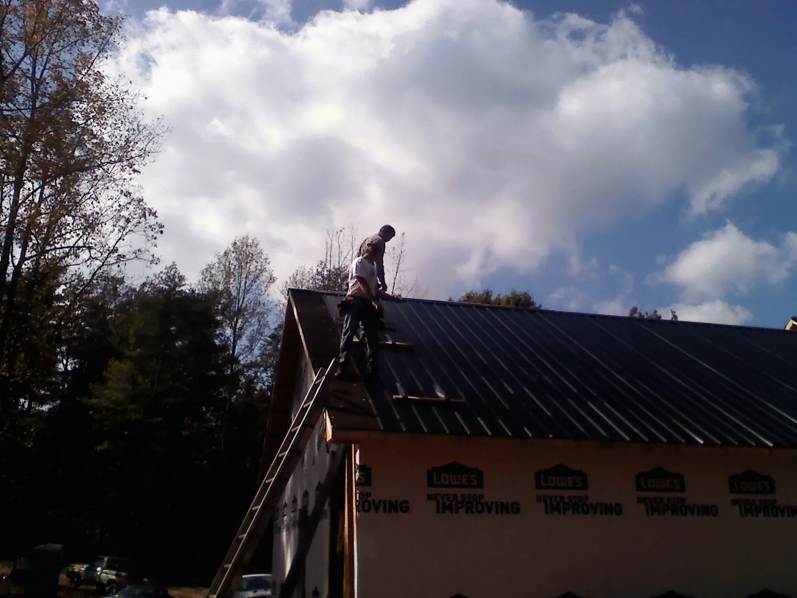 Roofer fastening dark metal panels high against a cloudy sky, from a Roof Inspection job in East Greenwich