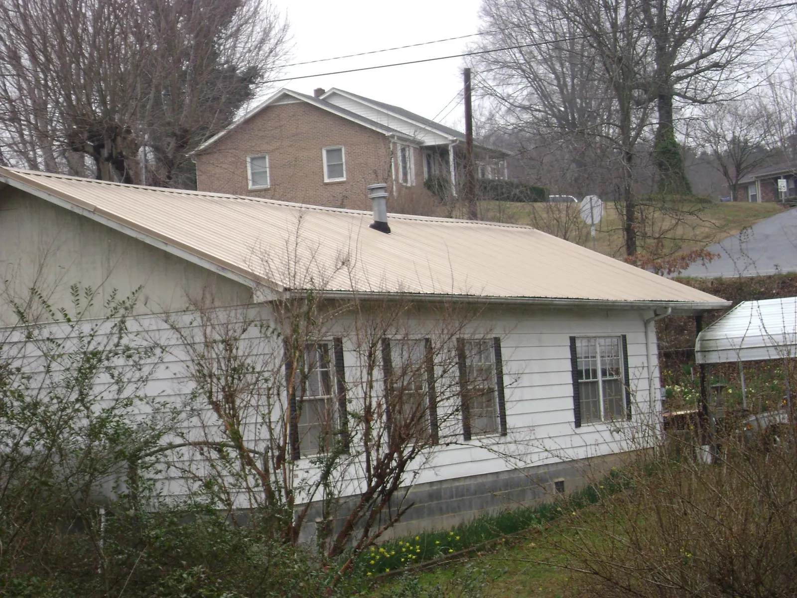 Tan metal roof on a white sided house set into a hillside — Commercial Roofing by Roofing Brothers in East Greenwich